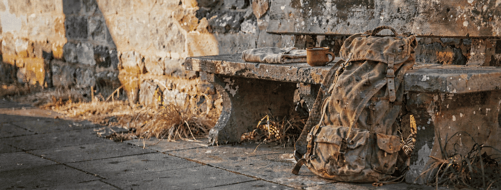 Schwerer Wanderrucksack abgestellt an einer Steinbank, daneben ein Becher Wasser.